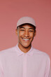 © BONNINSTUDIO/Stocksy - Man wearing pink shirt and cap smiling on pink background