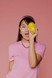 © BONNINSTUDIO/Stocksy - Woman holding lemons over eye on pink background