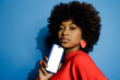 © BONNINSTUDIO/Stocksy - Woman holding smartphone with blank screen on blue background