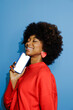 © BONNINSTUDIO/Stocksy - Happy woman holding smartphone against blue background