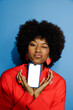 © BONNINSTUDIO/Stocksy - Woman holding smartphone making funny face on blue background