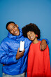 © BONNINSTUDIO/Stocksy - Couple showing smartphone screen smiling over blue background