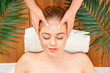 © Prostock-studio - Cosmetology and facial massage in spa. Girl lies on wooden table on white towel, with palm leaves, top view, close up