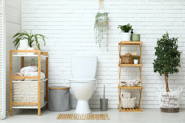 Wall Mural - Interior of modern restroom with ceramic toilet bowl, houseplant and shelving unit near white brick wall