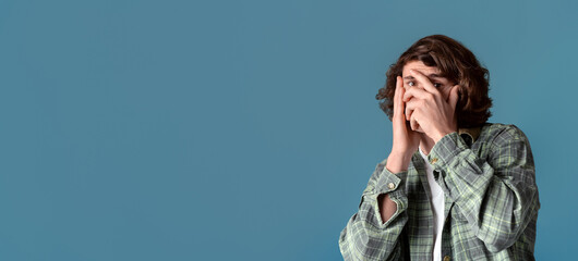 Wall Mural - Anxiety and stress concept. Curly guy closing his face in fear on color background