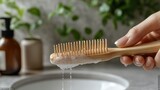 A hand holding a wooden comb with soap bubbles over a sink.