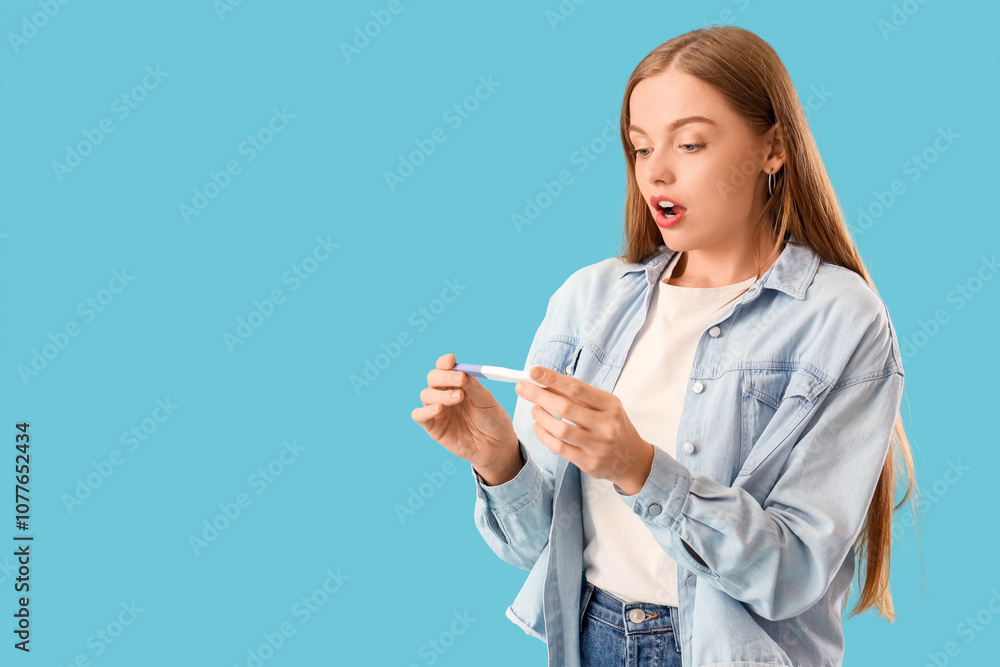 Shocked young woman with pregnancy test on blue background