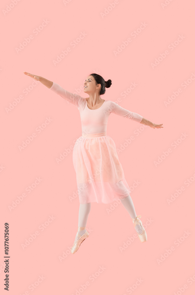 Young female ballerina jumping on pink background