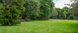 © Doublelee - Panoramic background texture of a lush green lawn surrounded by diverse mature trees. Peaceful landscaped garden with large outdoor space. Copy space for design.
