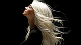 A female in her 30s with lush beautiful blonde hair, minimalism studio portrait, hair blowing in the wind, eyes closed. Profile view of glamorous young woman model wearing black. Wind blowing.