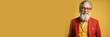 © Ruslan - banner fashionably dressed gray-haired old smiling man with a long beard in bright glasses in a bright red colorful suit on a yellow background cinematic light with empty space for text or design
