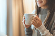 © oatawa - Close up of women's hands holding white cup mug in winter with copy space advertising text message, sweet coffee or tea.