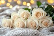 © DudeDesignStudio - A bouquet of six cream-colored roses laid on a white knitted blanket with a bokeh background.