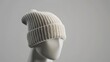 © Muhammad - Closeup of a white knitted beanie on a mannequin head against a grey background.