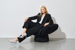 © boomeart - Modern businesswoman in black pantsuit sits on black bean bag