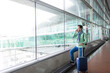 © Cavan Images - Man standing next to airport hall window while using a mobile phone