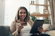 © peopleimages.com - Home, woman and smile with credit card on tablet for flight tickets or accommodation payment for holiday. Female person, apartment and portrait in living room on sofa with online shopping or discount