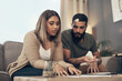 © N F/peopleimages.com - Home, couple and reading with legal documents for mortgage or loan agreement on sofa. Apartment, people and serious together in living room with paperwork, form and contract for life insurance
