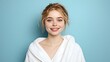 © nilawan - Smiling young woman in a cozy robe poses against a blue background for a refreshing look