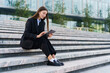 © muse studio - Young Professional in a Black Suit Sits on Steps Using a Tablet Outside a Modern Building During Daylight