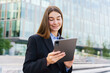 © muse studio - Professional Woman Using a Tablet Outdoors Near a Modern Office Building in Bright Daylight