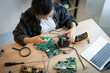 © Thanadon88 - A woman is working on a computer part. She is wearing a white shirt and a black jacket