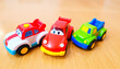 © alexrona - Three colorful toy cars lined up on a wooden surface, representing children’s play and vehicle toys.