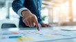 © kokoson6 - A business professional points at a strategy map on a table, highlighting key data and insights in a modern, bright office space.
