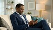 © Tariq - African Businessman Using Mobile Phone on Sofa, Professional at Home,Modern African Businessman Relaxing on Sofa with Mobile Phone, Business at Home