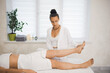 © junky_jess - Lymphatic drainage massage. Masseuse in white outfit lifts the leg of the woman client who lying on back on the couch, selective focus.