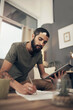 © N F/peopleimages.com - Home, man and tablet with paperwork for finance, track expenses or planning for budget goal on sofa. House, male person or financial with writing for payment review, digital savings or mortgage bills