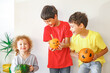 © Olga Gimaeva - Three real siblings standing together against white wall at cozy home and holding in their hands three orange and green pumpkins with scary faces, happy halloween at home