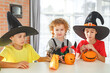 © Olga Gimaeva - Three real happy siblings two brothers and sister cutting together from real natural pumpkin jack o lantern, while playing with paper decorations of ghosts, children wearing with witch hats, halloween