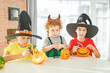 © Olga Gimaeva - Three real happy siblings two brothers and sister cutting together from real natural pumpkin jack o lantern, while playing with paper decorations of ghosts, children wearing with witch hats, halloween