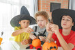 © Olga Gimaeva - Three real siblings two brothers and sister making together jack o lantern at their home white kitchen, cutting real pumpkins and playing with paper black ghosts, lovely vibe of halloween