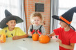 © Olga Gimaeva - Three real siblings two brothers and sister making together jack o lantern at their home white kitchen, cutting real pumpkins and playing with paper black ghosts, lovely vibe of halloween