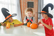 © Olga Gimaeva - Three real siblings two brothers and sister making together jack o lantern at their home white kitchen, cutting real pumpkins and playing with paper black ghosts, lovely vibe of halloween