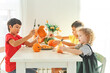 © Olga Gimaeva - Three real happy siblings two brothers and sister cutting together from real natural pumpkin jack o lantern, while playing with paper decorations of ghosts, children wearing with witch hats, halloween
