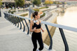© BGStock72 - Morning run along the riverwalk in a bustling urban park, showcasing an energetic woman enjoying her fitness routine and nature's beauty