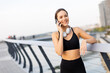 © BGStock72 - Young woman enjoying a call while taking a break from her jog at a tranquil riverside promenade during a sunny afternoon