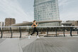 © BGStock72 - A woman jogging along a modern sidewalk, surrounded by sleek buildings and urban scenery on a clear day
