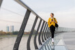 © BGStock72 - Cheerful woman strolls along a modern bridge, chatting on her phone while enjoying the serene cityscape at dusk by the water
