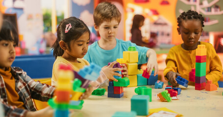 Wall Mural - Group of Adorable Creative Kids Using Colorful Building Blocks to Play Together. Cheerful Female Teacher Spending Productive Time in Daycare, Teaching Multiethnic Kids in Preschool