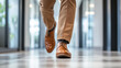 © Sawyer0 - Stopy mężczyzny w eleganckim brązowym garniturze poruszają się po korytarzu biurowym w pośpiechu, zmierzając na spotkanie.