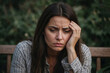© polack - Portrait of sick woman with a headache sits on a bench in a park