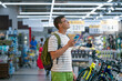 © wifesun - Young man with backpack using mobile phone choosing bicycle in sporting goods store reading reviews and comparing prices