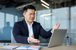 © Tetiana - Angry young Asian male businessman sitting at desk in office and looking frustrated at laptop screen gesturing with hands