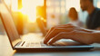© Bonsales - Hands typing on laptop keyboard in modern office with colleagues working in background during sunset