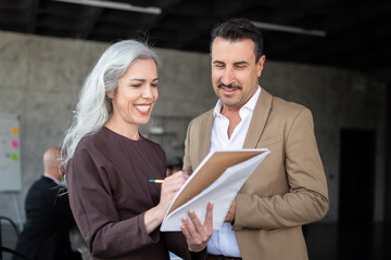 Fototapete - A woman and a man engage in a collaborative discussion in a modern office. The woman writes on a notepad while the man listens attentively, both smiling as they share insights.