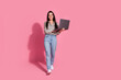 © deagreez - Young woman with brunette hair in casual jeans and a striped shirt holds a laptop against a vibrant pink background, smiles confidently